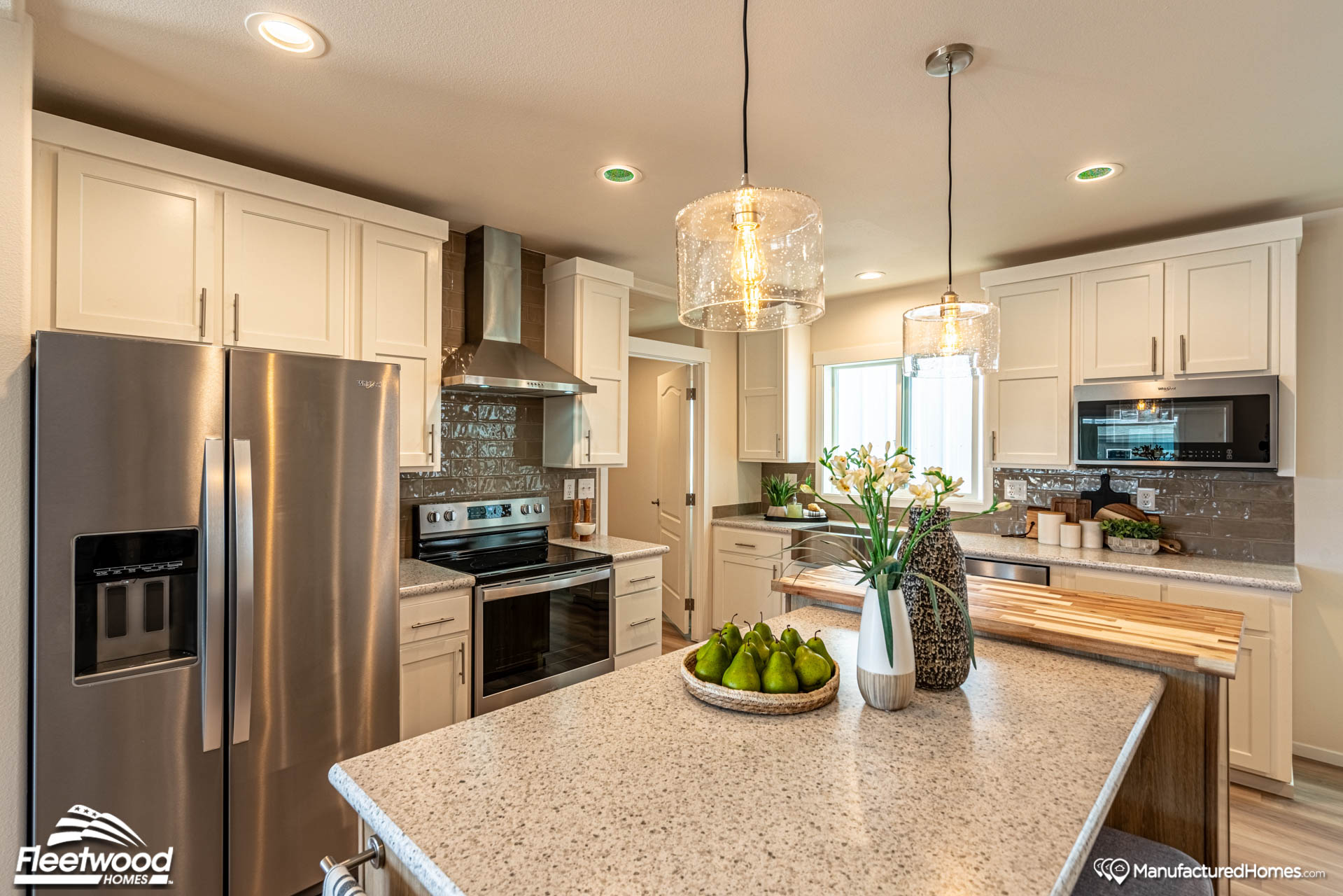 Modern kitchen with white cabinets, stainless steel appliances, and pendant lighting. Center island features decorative pears and flowers. Bright, clean design.