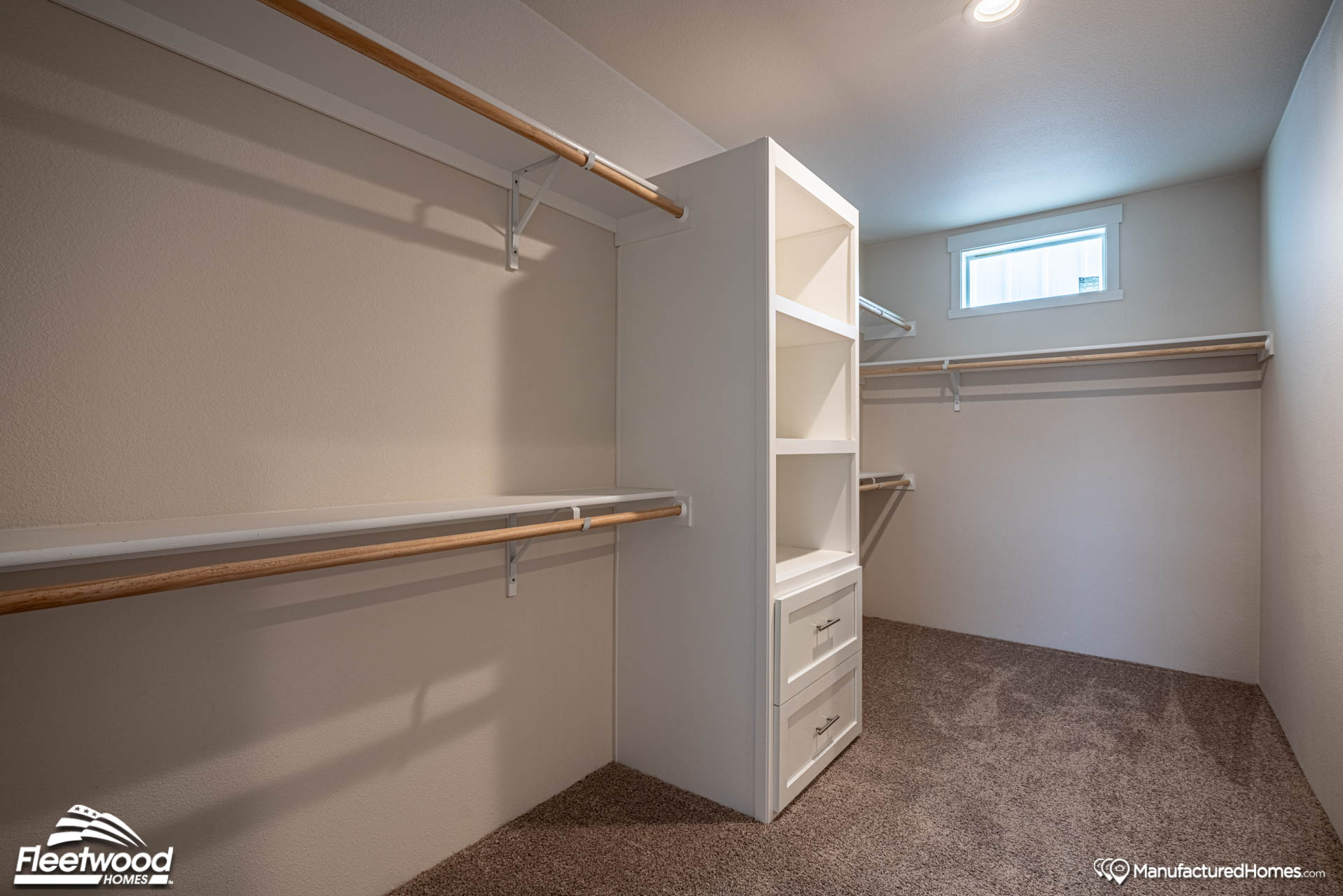Spacious walk-in closet with beige walls, carpeted floor, wooden shelves, and rods for hanging clothes. Light enters through a small window. Cozy and organized atmosphere.