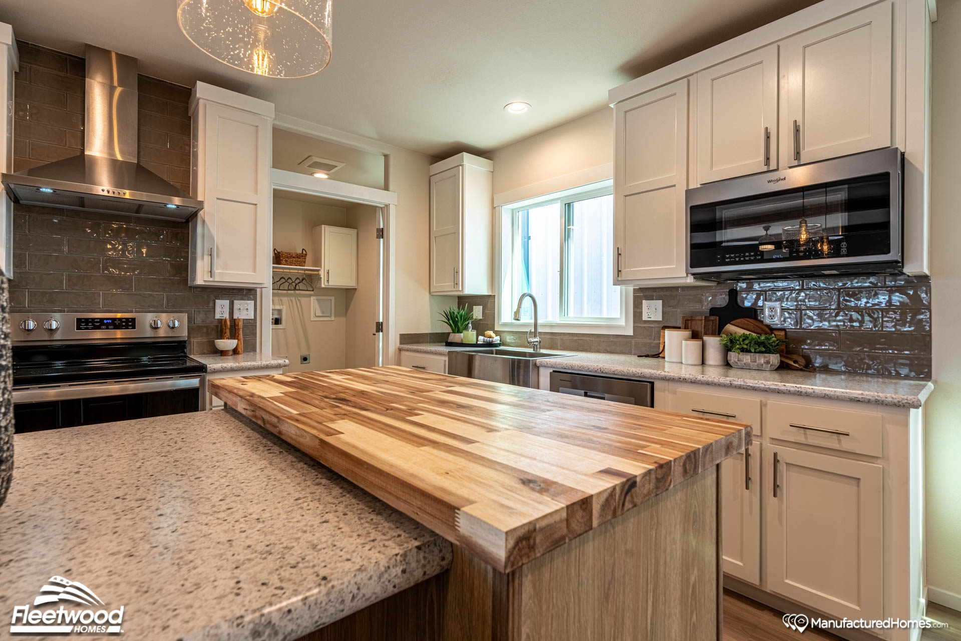 Modern kitchen with light wood cabinets, a butcher block island, and granite countertops. Stainless steel appliances and a window add brightness.