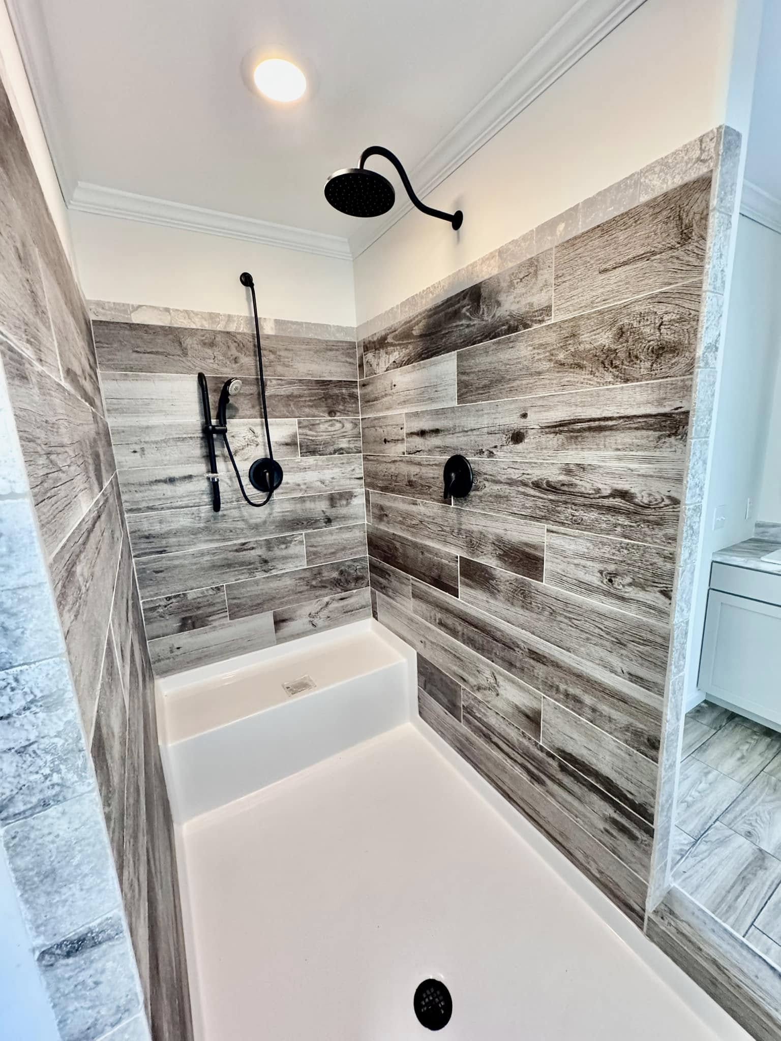 Stylish shower with rustic wood-patterned tiles, black fixtures, and a bright ceiling light. The space feels modern and inviting.