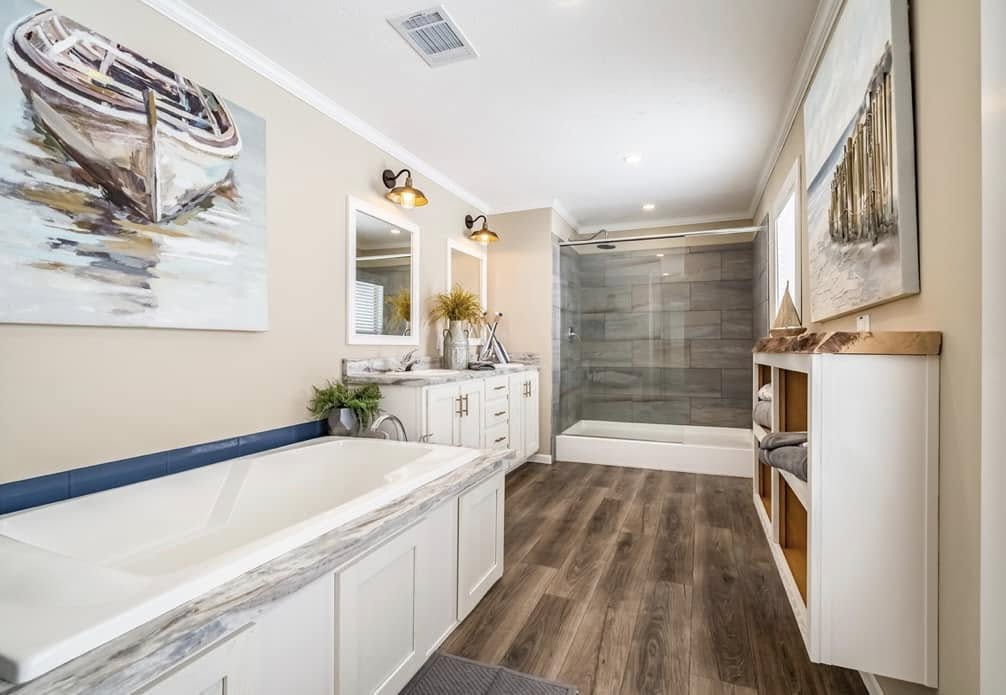Stylish bathroom with wood floors, large bathtub, and glass shower. Art of a boat on beige walls adds a serene touch, complemented by soft lighting.