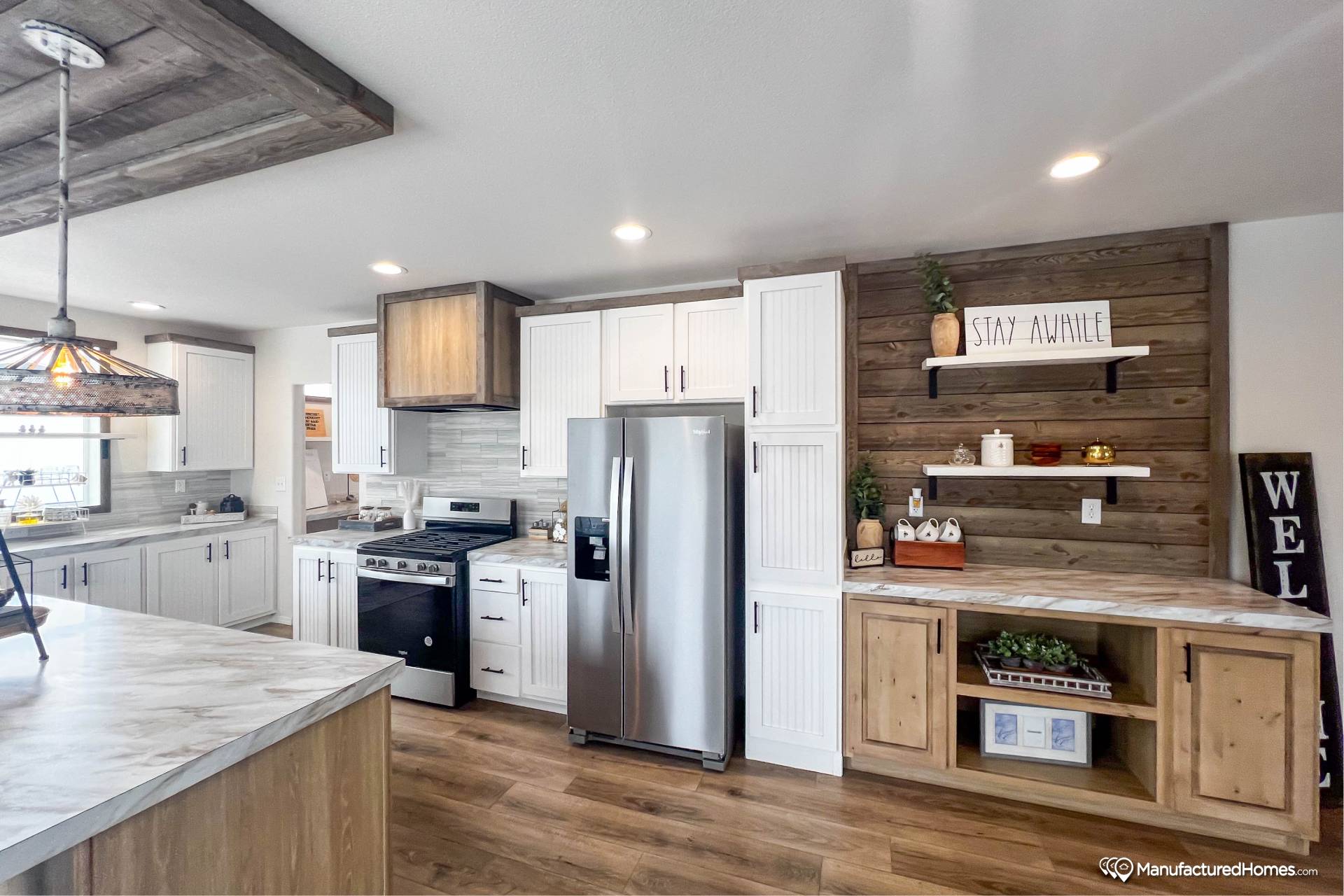 Modern kitchen with wood and white cabinets, stainless steel appliances, and marble countertops. Shelving displays jars and decor with a cozy feel.