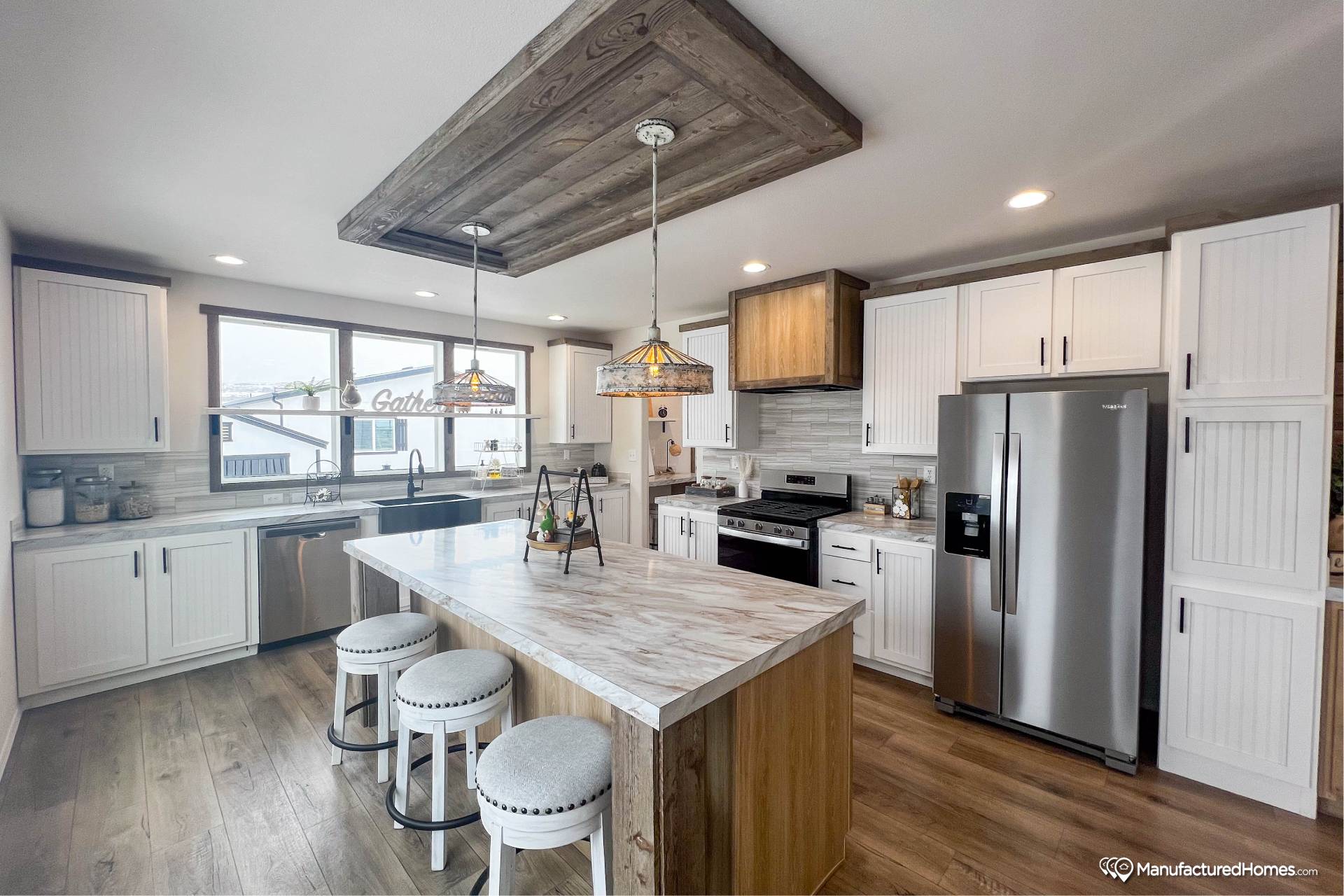 Modern kitchen with a marble island, three stools, and wood accents. Features white cabinets, stainless steel appliances, and warm pendant lighting.