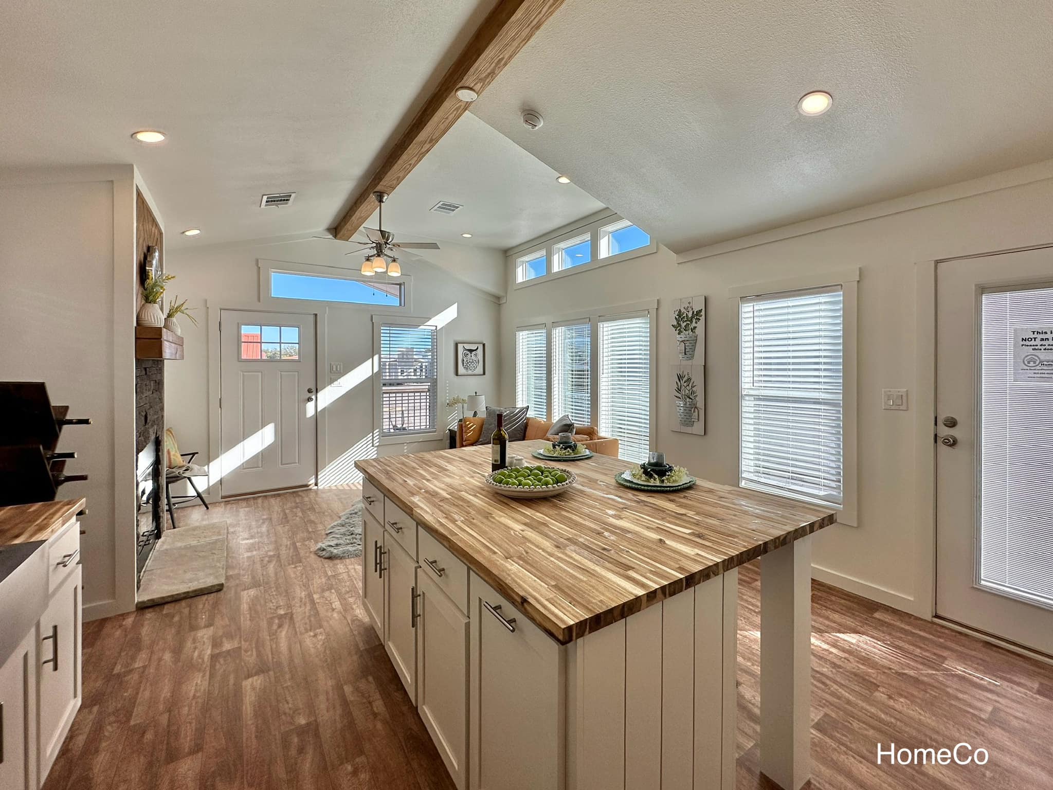 Bright, modern kitchen with wood flooring and a large island. Sunlight streams through tall windows, highlighting cozy seating and decor.