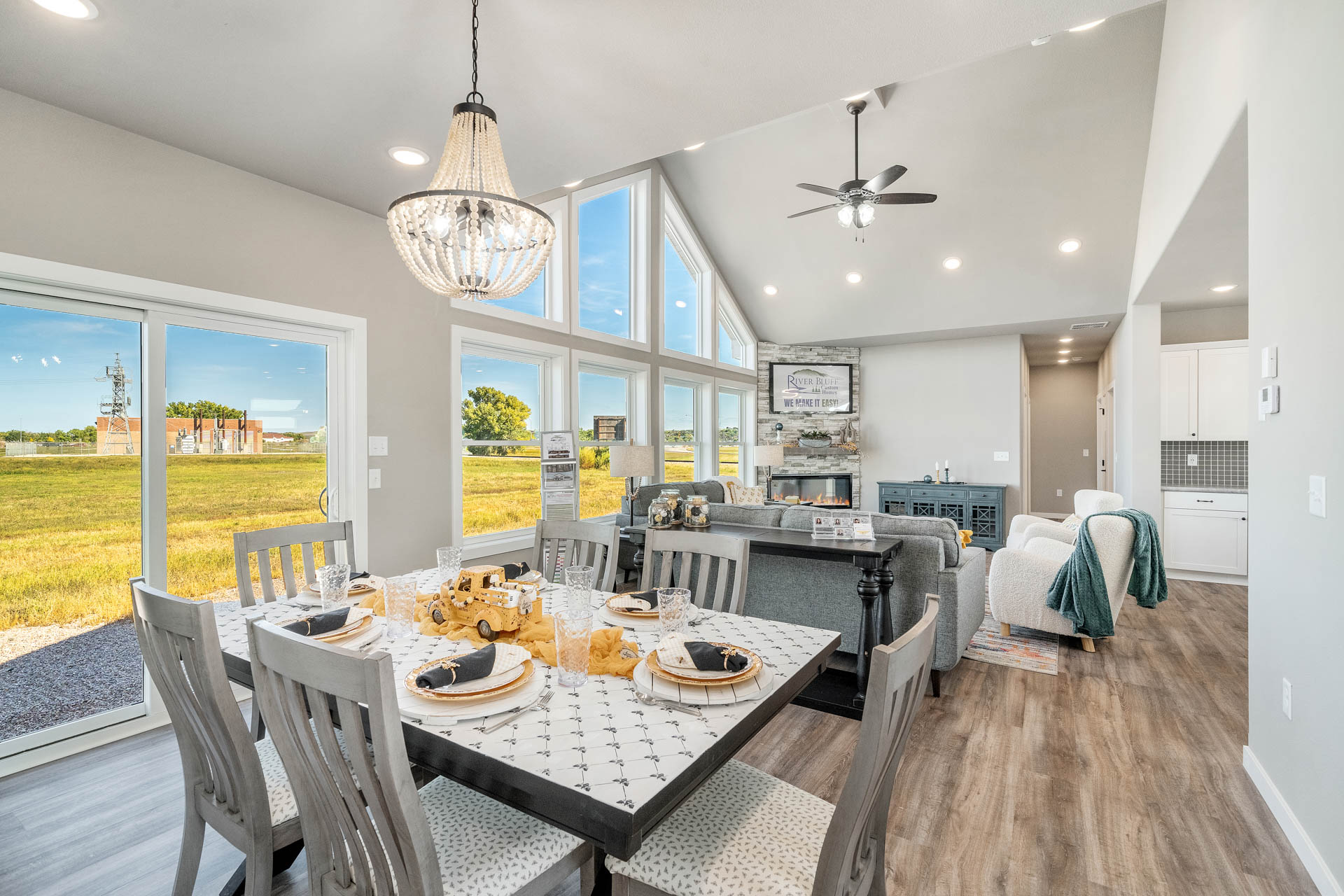 Bright, modern living and dining area with wooden floors, a decorative dining table set for six, large windows, and a cozy living room with a fireplace.