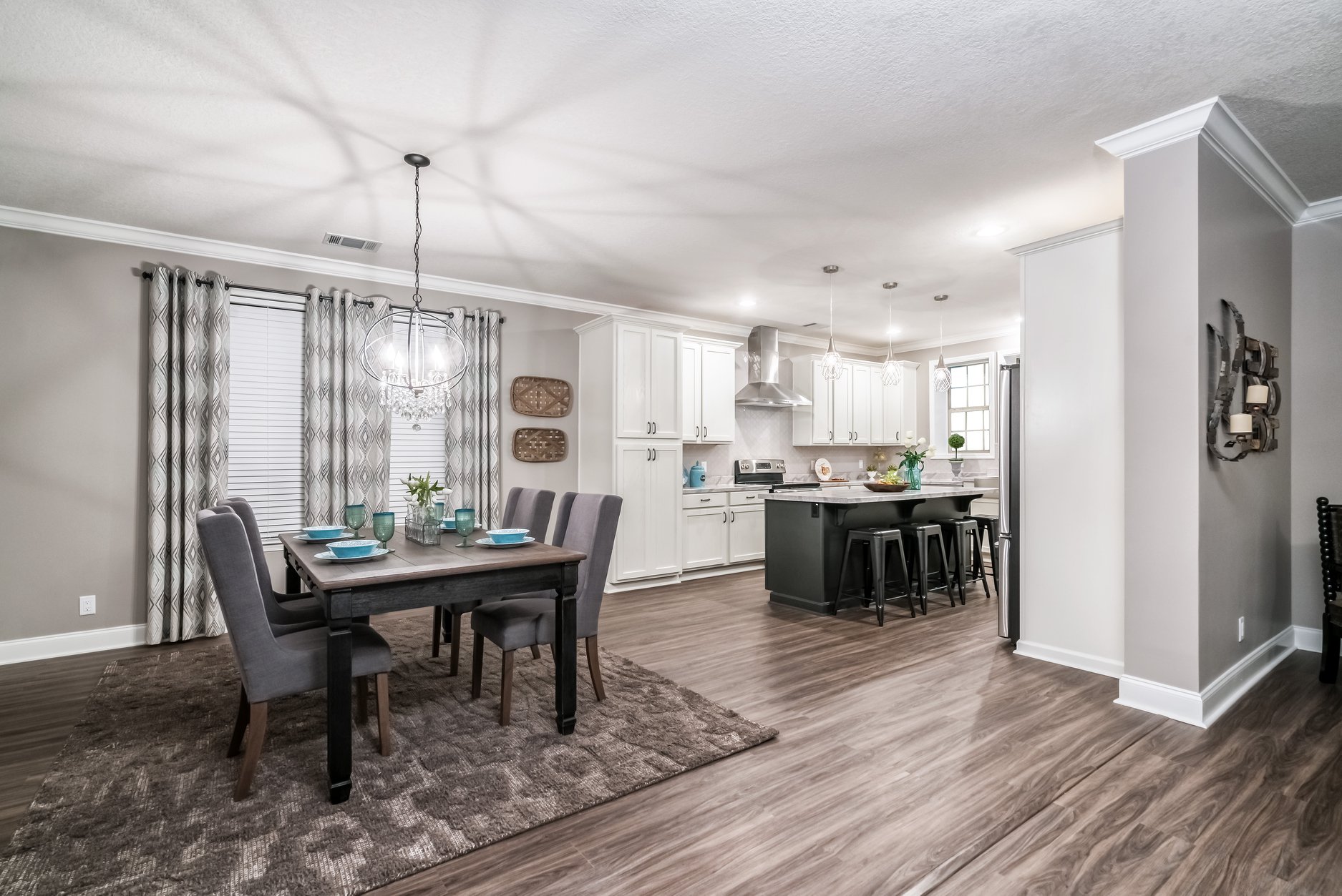 Modern dining and kitchen area with hardwood floors. Features a dark wood table set for four, a chandelier, white cabinets, and a kitchen island with bar stools. Cozy and inviting ambiance.