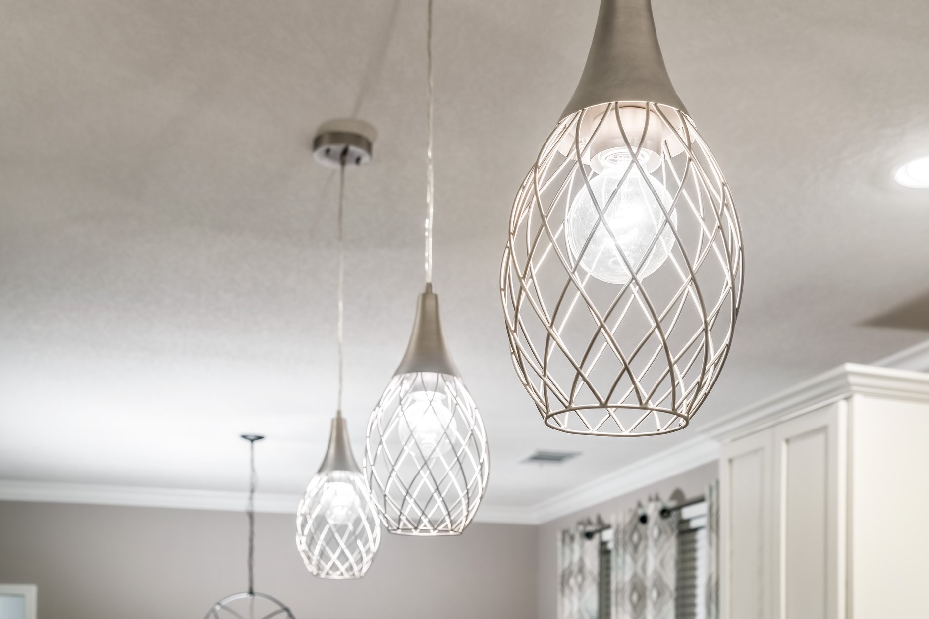 Modern ceiling lights with sleek, metallic lattice designs hang in a neutral-toned room, casting soft, warm light and creating an elegant ambiance.