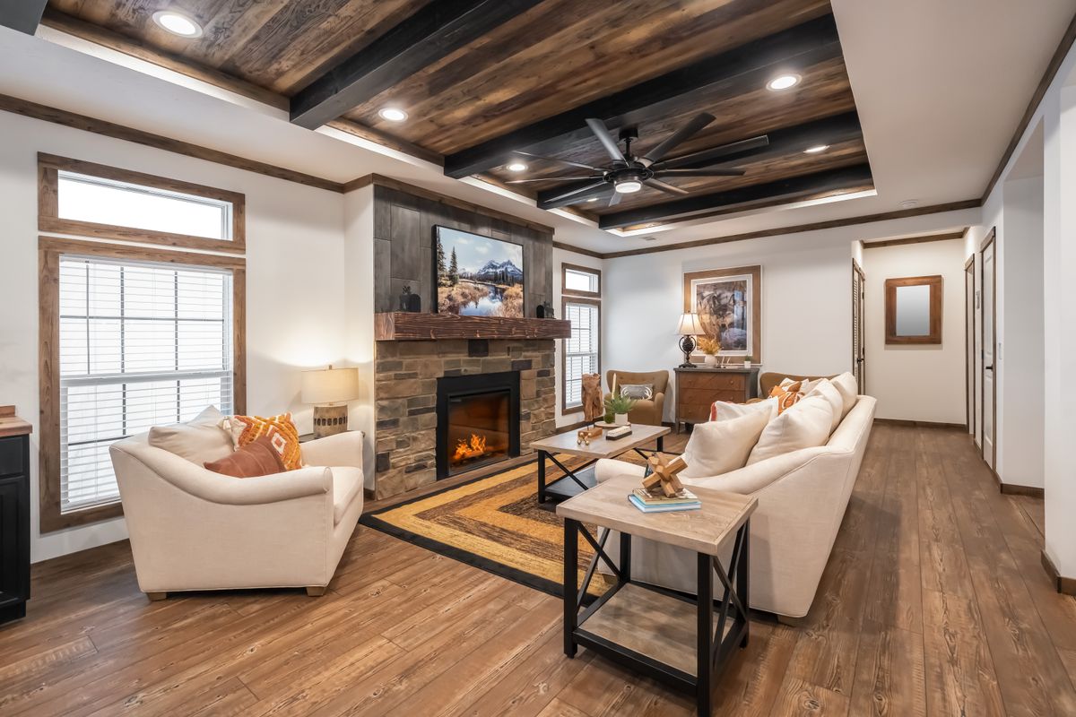Cozy living room with a wooden ceiling and floors, featuring a stone fireplace, neutral sofas, and a rustic coffee table, creating a warm, inviting ambiance.