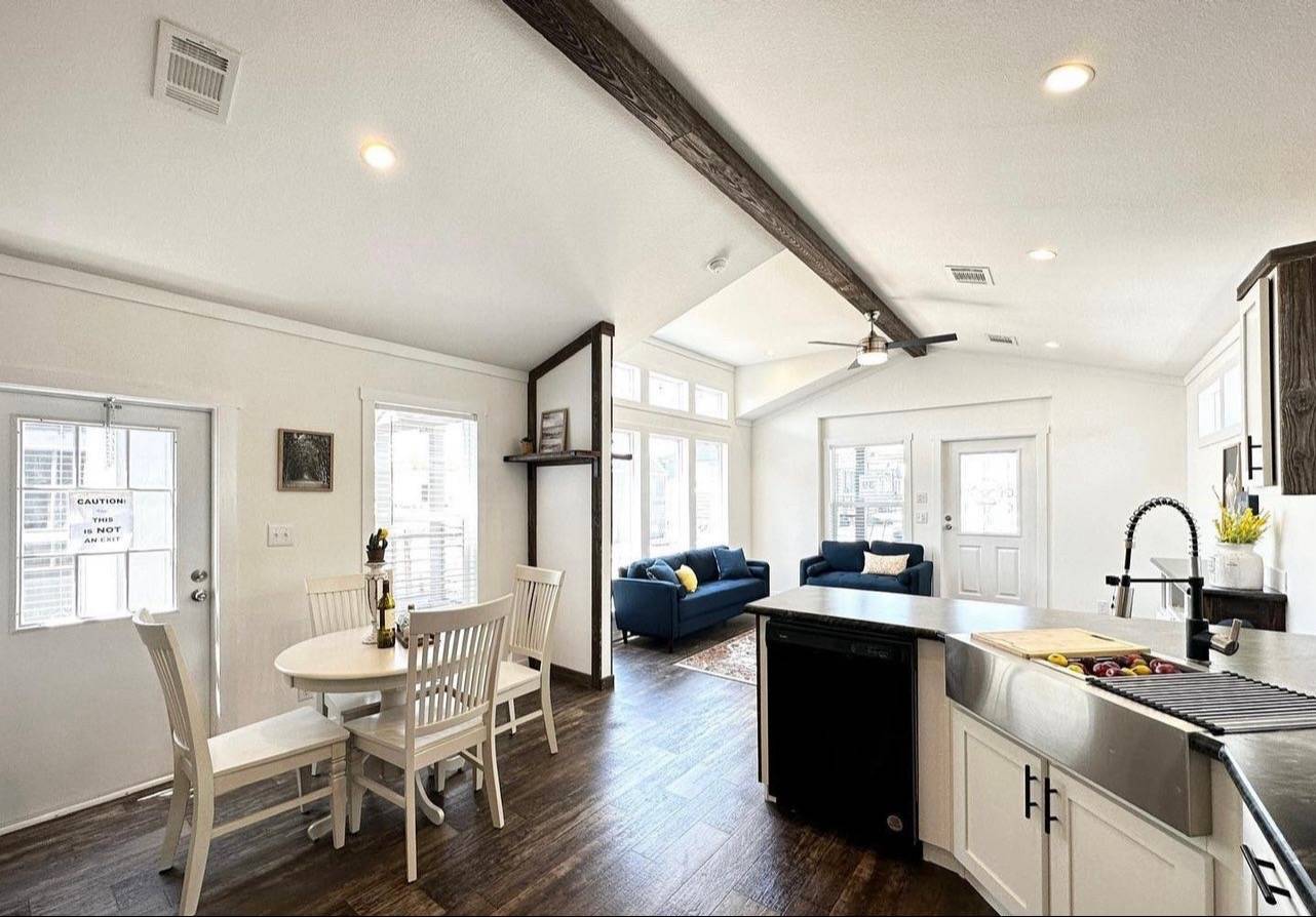 Bright, open-plan living area with vaulted ceiling. Features a round dining table, modern kitchen, and a cozy blue sofa, creating a welcoming atmosphere.