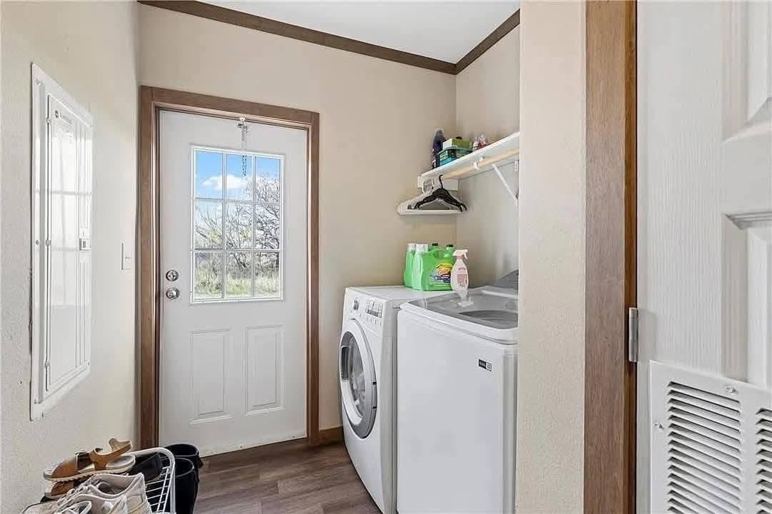 Laundry room with a washer and dryer next to a door with a window. A shelf above holds detergent and hangers, conveying a neat, functional space.