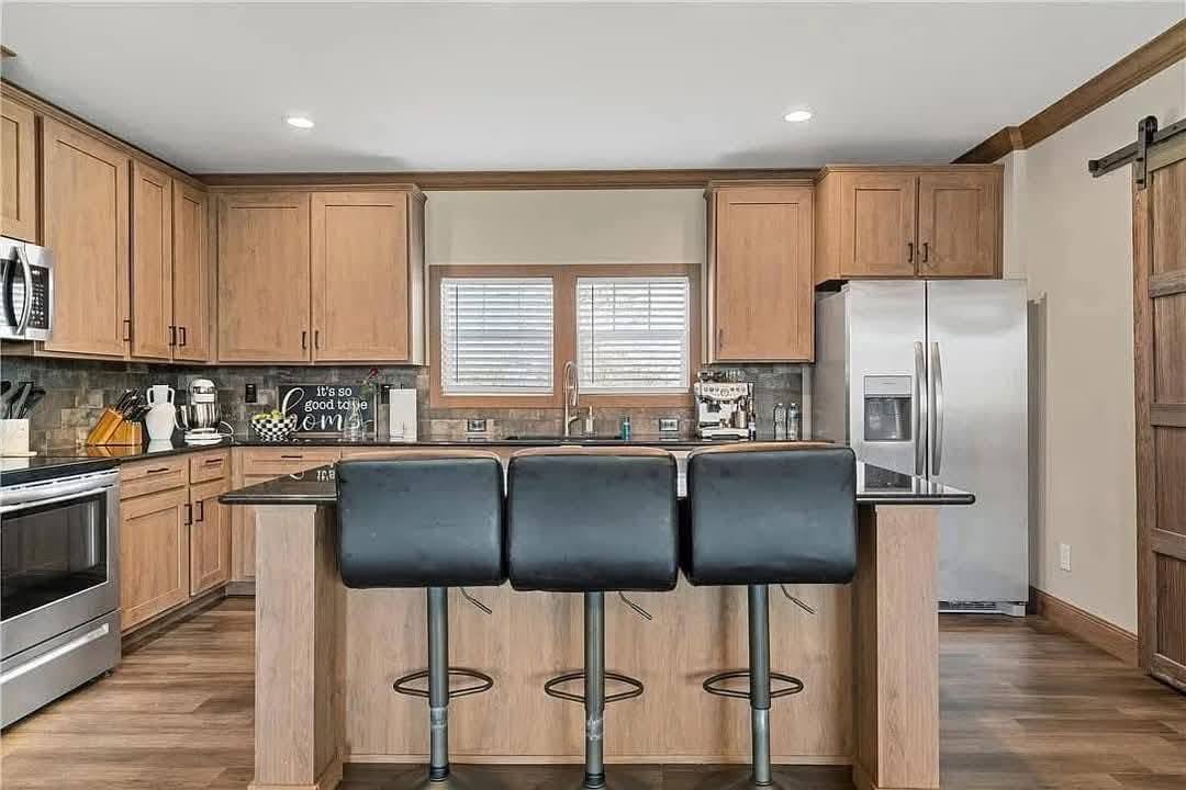 Warm, inviting kitchen with wood cabinets, stainless steel appliances, and a central island with three black bar stools. Cozy and modern ambiance.