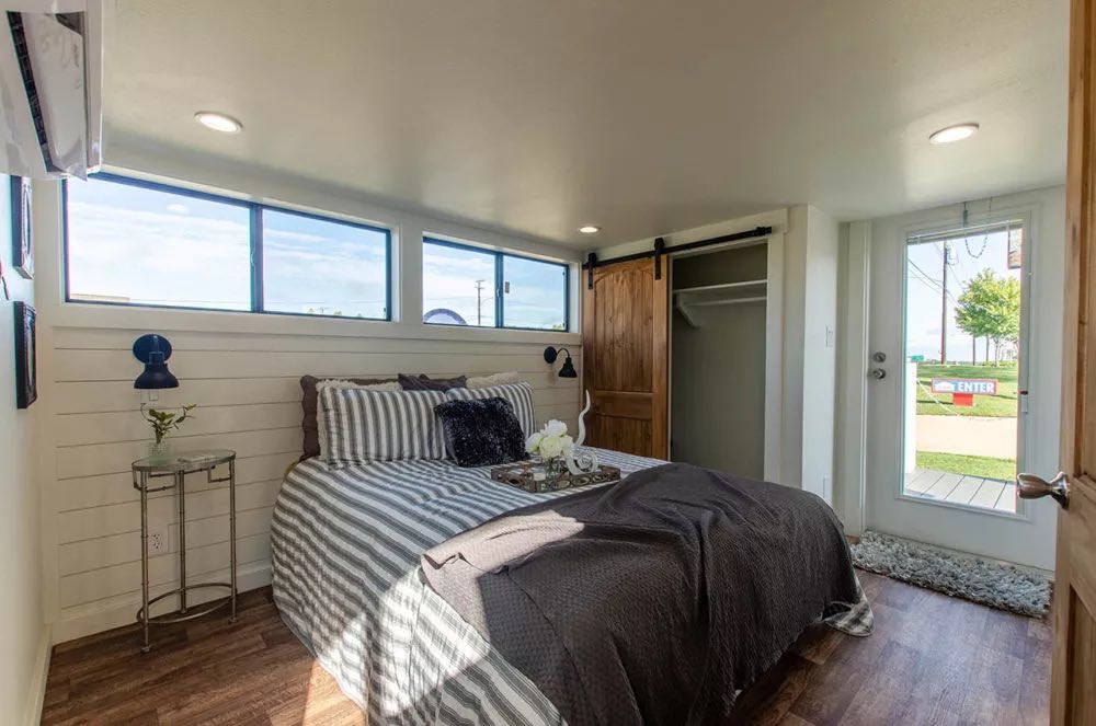 Cozy bedroom with a striped bed, dark bedding, and an ornate tray. Barn door closet, bright windows, and white walls create an airy, inviting atmosphere.