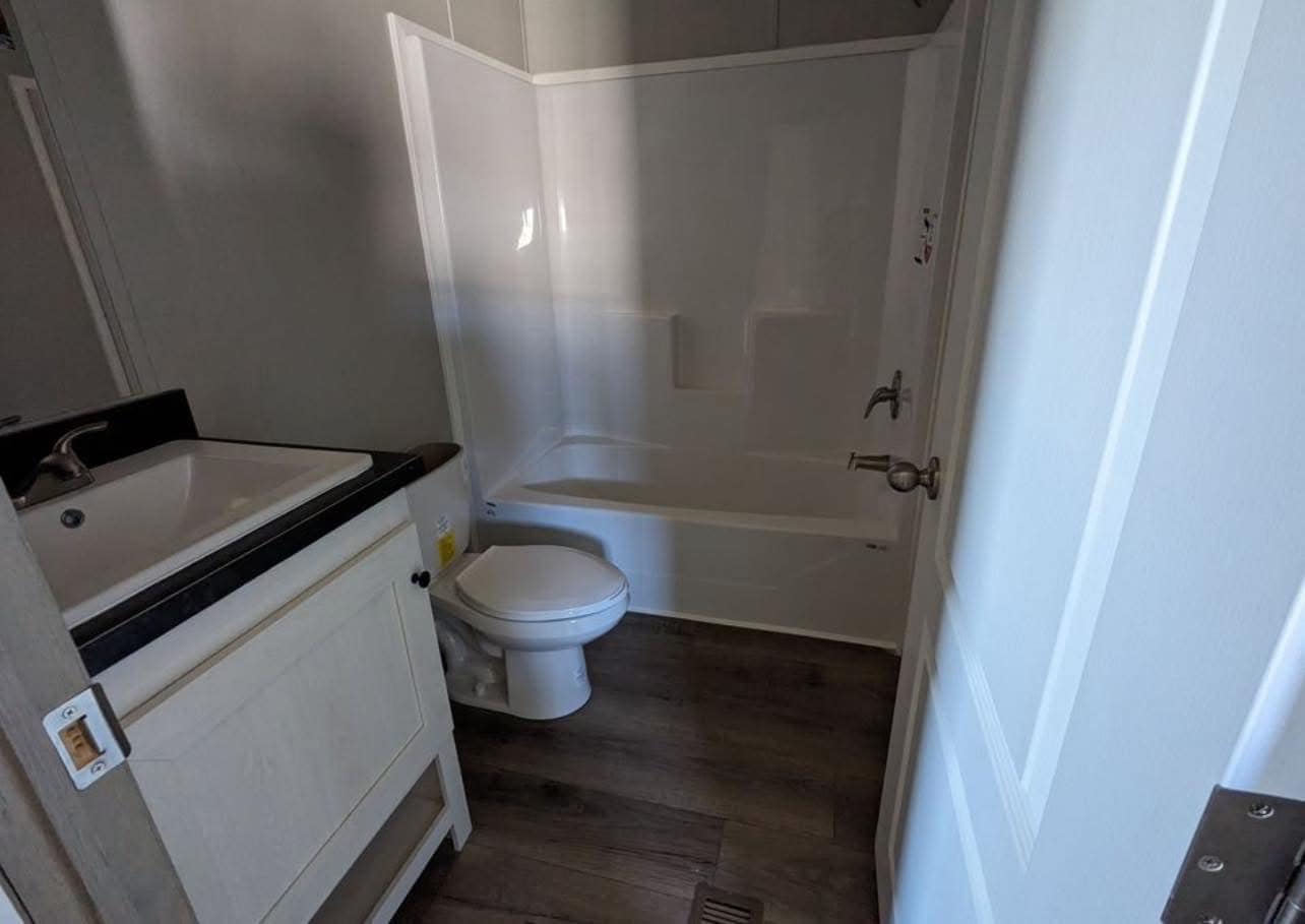 Small bathroom with white fixtures. Includes a bathtub-shower combo, toilet, and sink with a black countertop. Wooden floor adds warmth.
