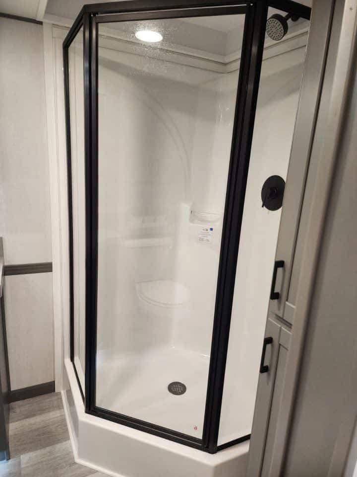 A modern bathroom shower with a glass enclosure and black metal frame. The shower area is white, and the design conveys a sleek, minimalist aesthetic.