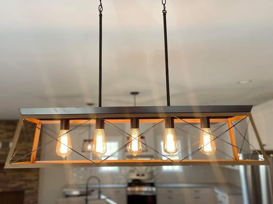 Modern rectangular pendant light with four exposed vintage-style bulbs, hanging in a bright kitchen. The ambiance is warm and inviting.