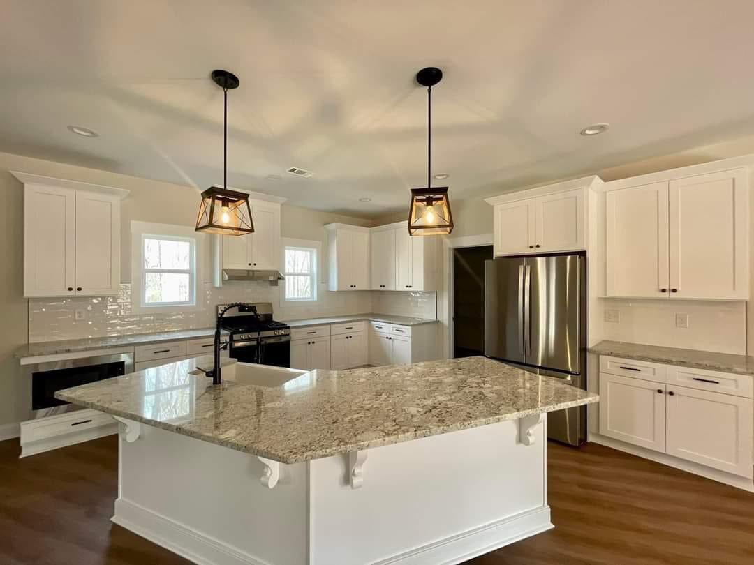 Spacious kitchen with white cabinets, granite countertops, stainless steel appliances, and two pendant lights over the island. Warm and inviting atmosphere.