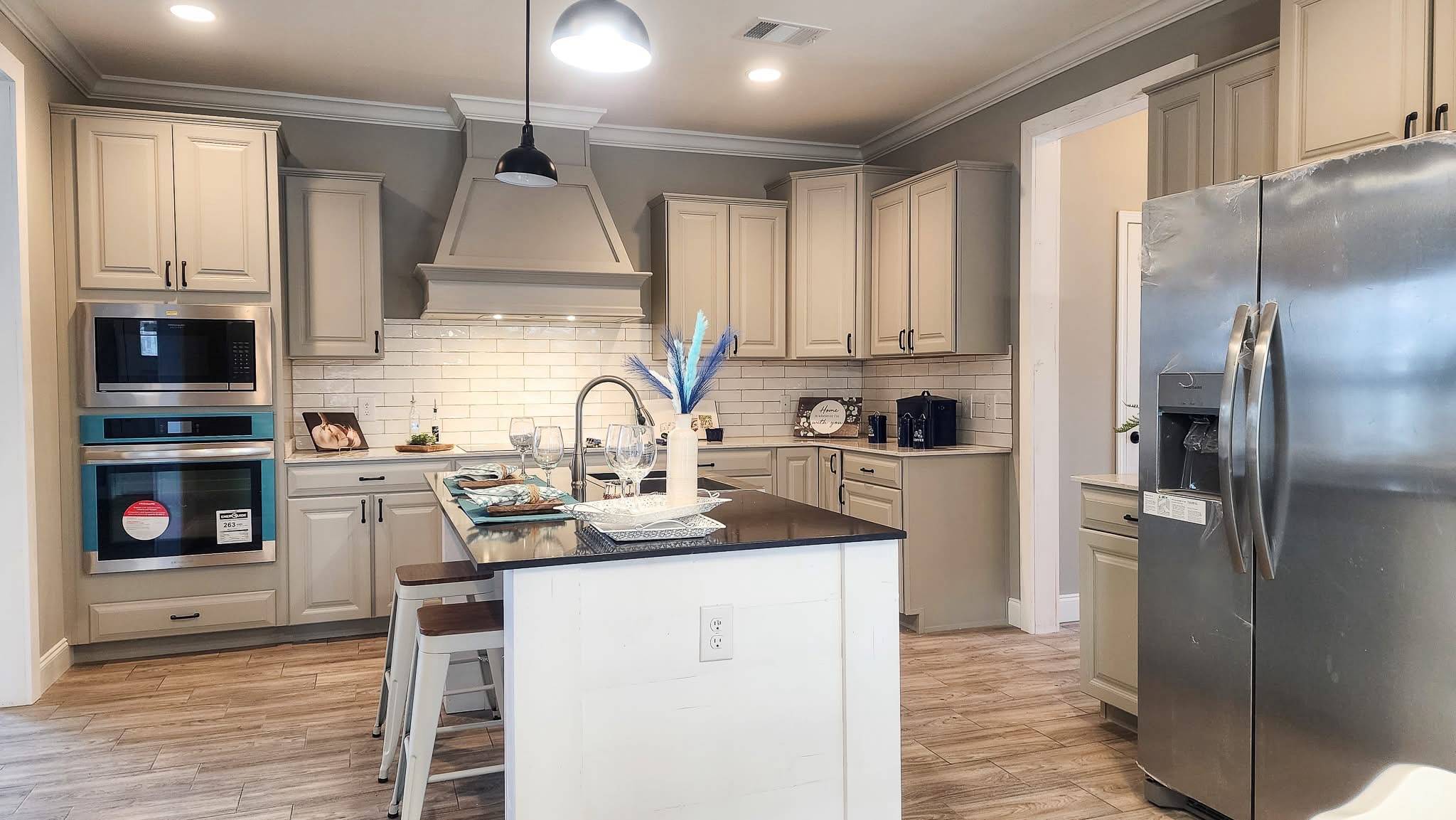 A modern kitchen with beige cabinets, stainless steel appliances, and a central island. The room is well-lit with a cozy and inviting atmosphere.