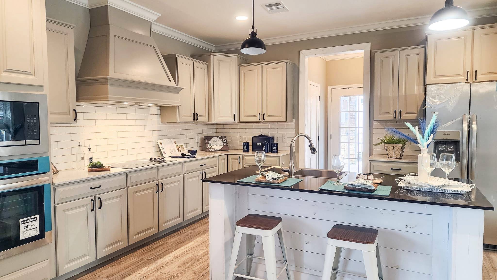 Bright kitchen with beige cabinets, stainless steel appliances, and a black island. Two stools and neatly set placemats create a welcoming feel.