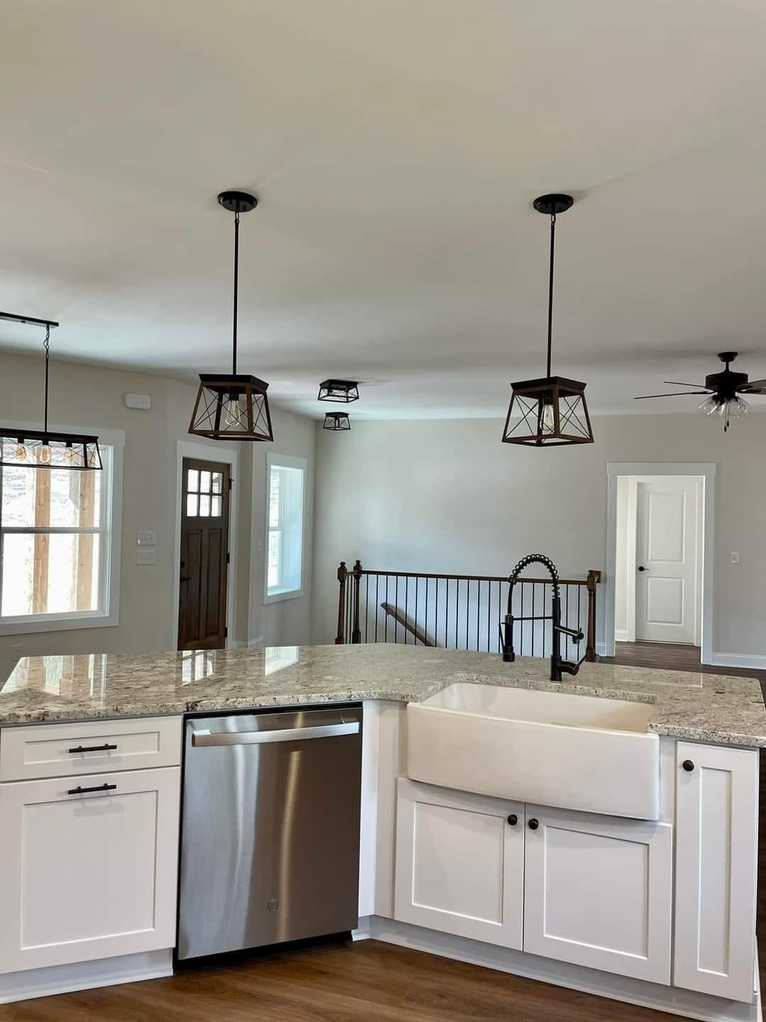 Modern kitchen with white cabinets, granite countertops, farmhouse sink, and stainless steel dishwasher. Pendant lights and a ceiling fan add elegance.