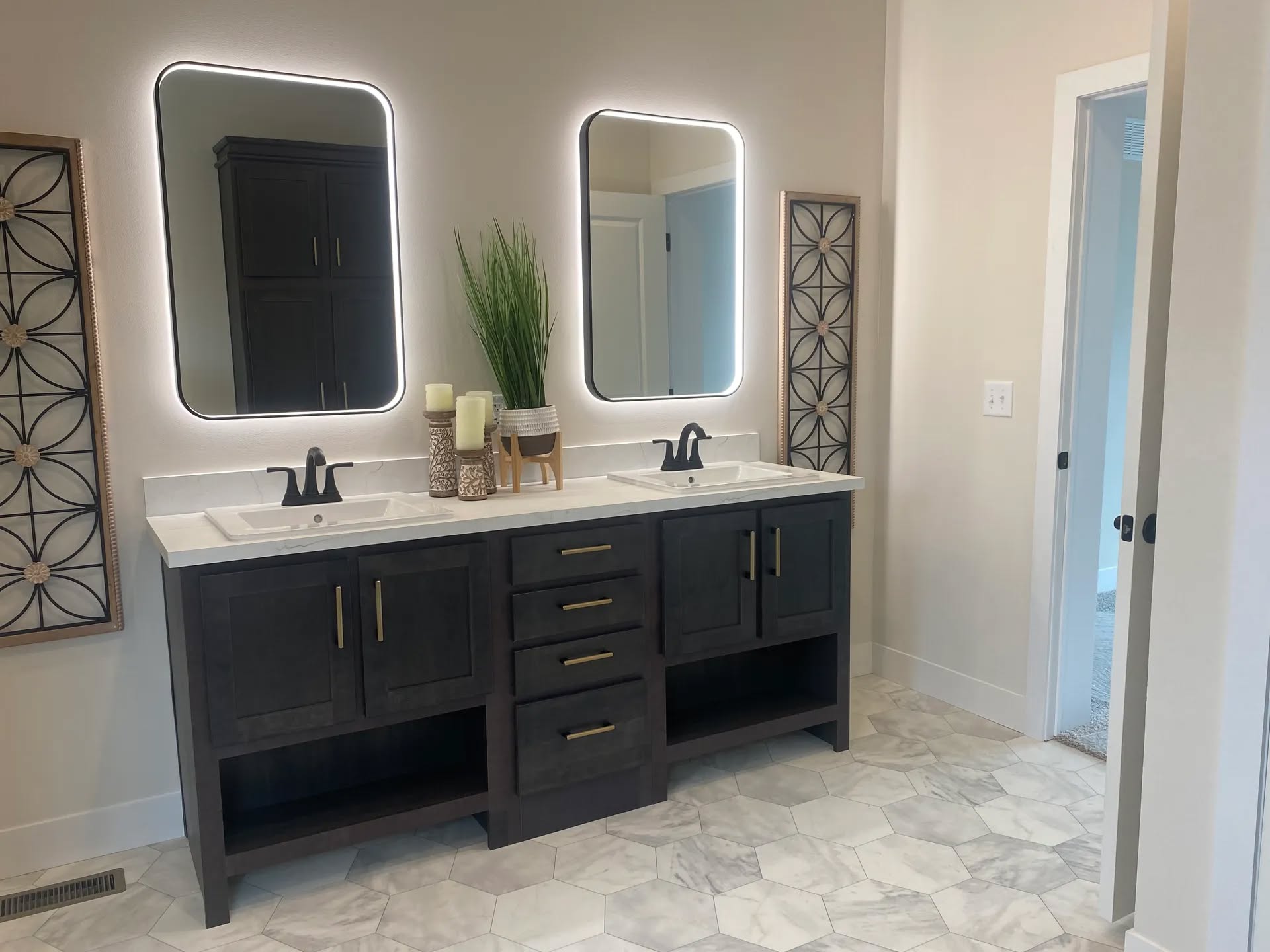 Modern bathroom with dual sinks and dark wooden vanity. Two backlit mirrors hang above, with decorative panels and candles adding elegance. Bright, airy feel.
