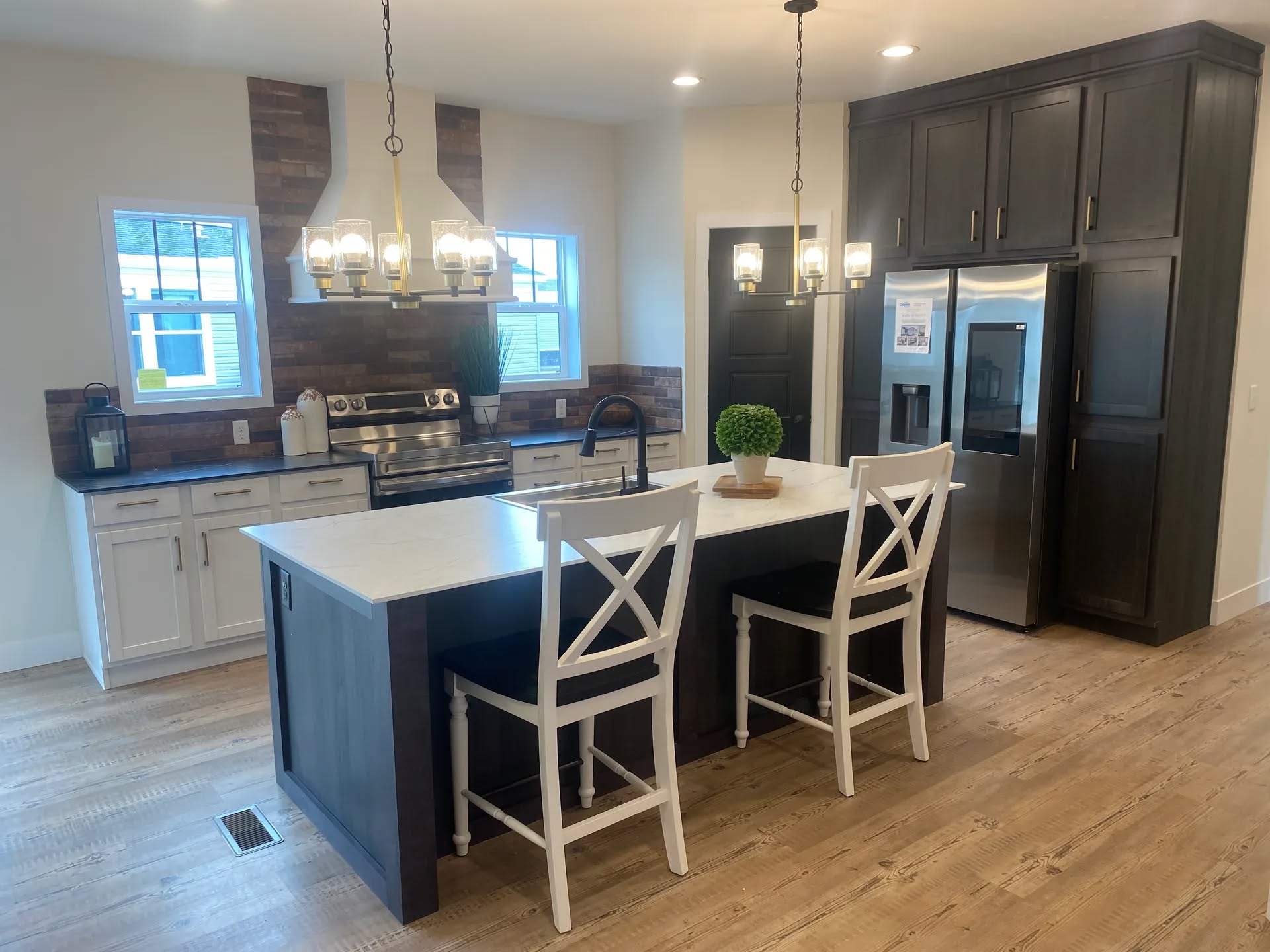 Modern kitchen featuring a central island with a white countertop and two high-backed white chairs. Dark wood cabinets contrast with stainless steel appliances. Bright, cozy atmosphere.