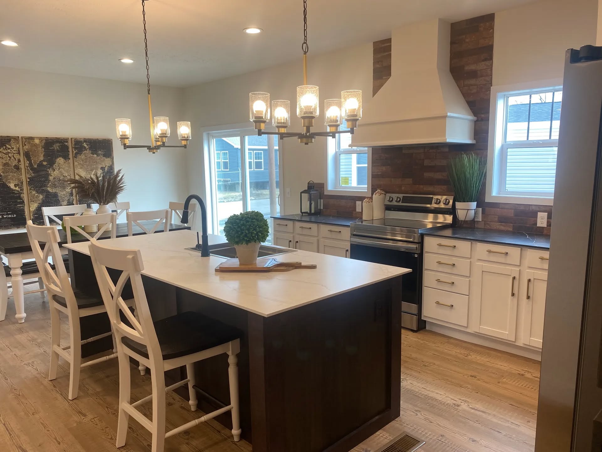 Modern kitchen with a central island, white cabinets, dark countertops, and wood accents. A chandelier hangs above. Bright and inviting ambiance.