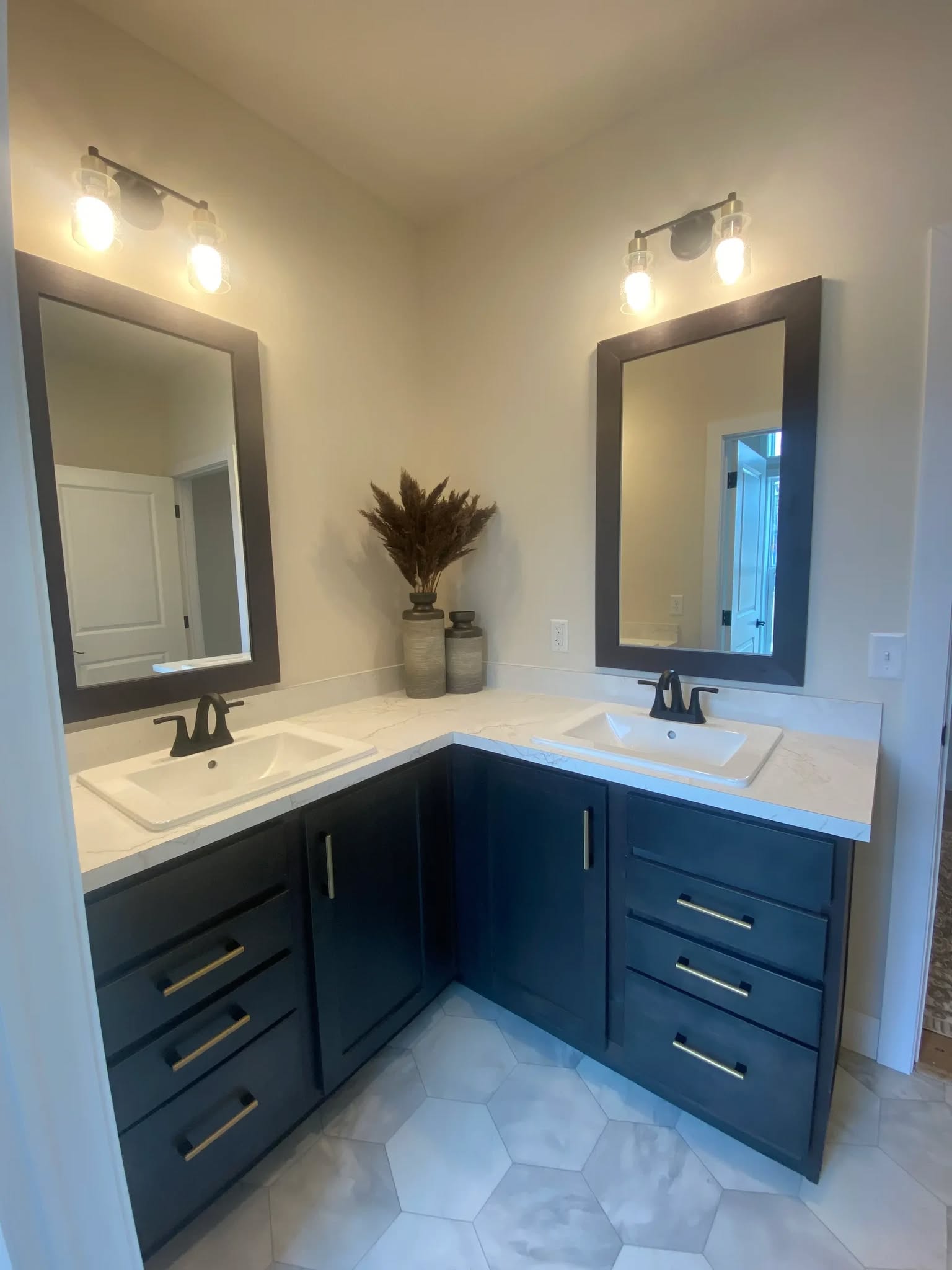 Modern bathroom with a dark wood corner vanity featuring two white sinks and black faucets. Two mirrors and wall lights enhance the clean, elegant look.