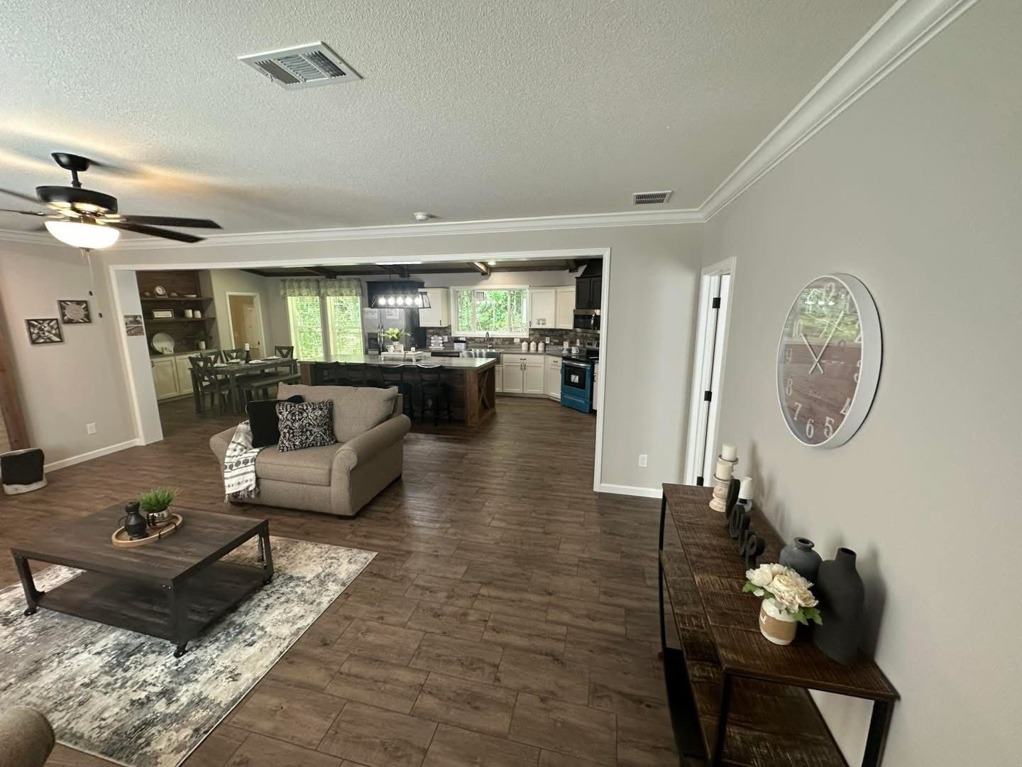Spacious open-plan living area with a modern kitchen. Features wood floors, a ceiling fan, cozy seating, and stylish decor. Bright and inviting atmosphere.