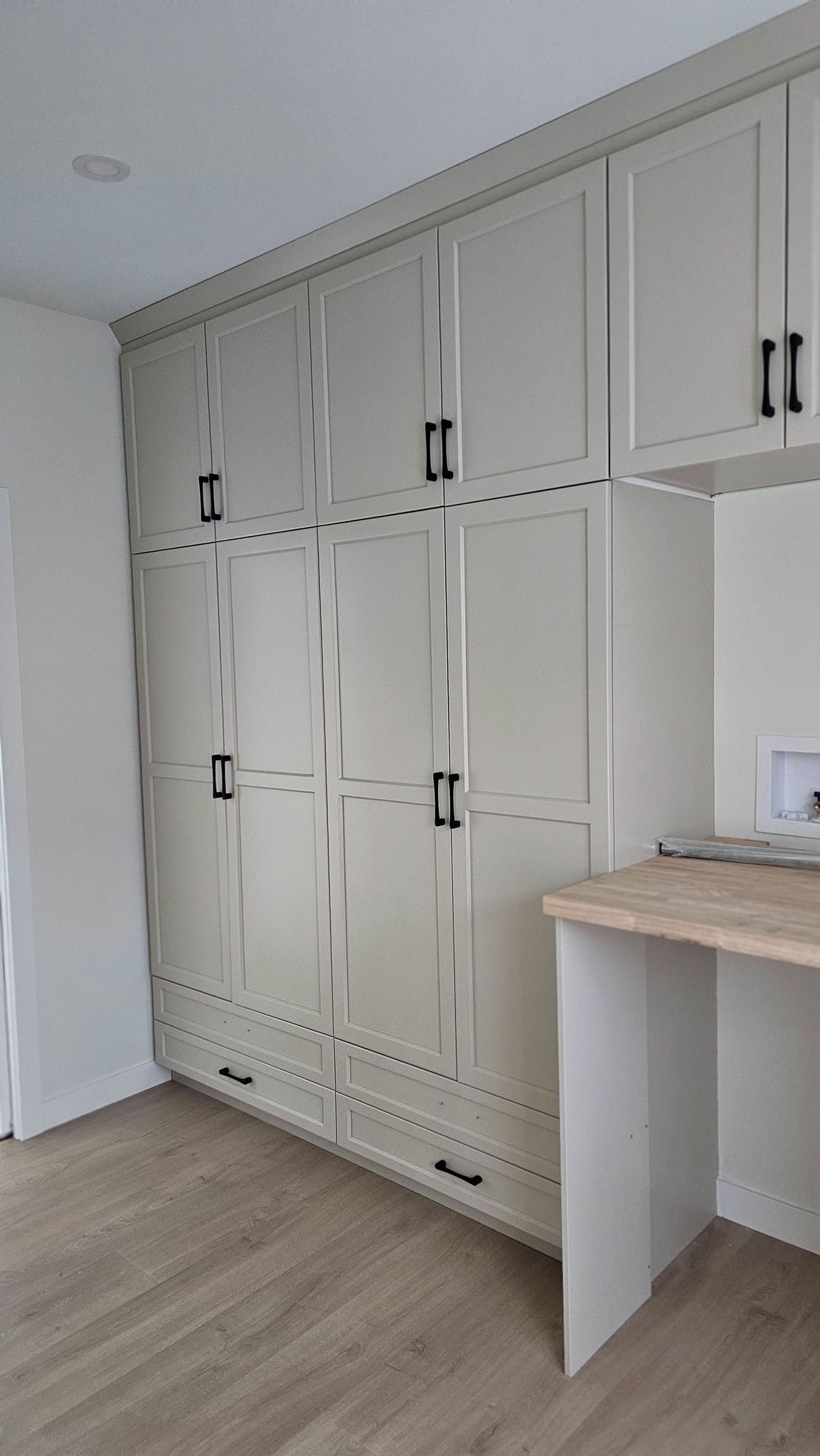 Built-in storage cabinets in a neutral-toned room. The cabinets feature sleek, modern black handles and a light wood countertop, conveying a minimalist, organized feel.