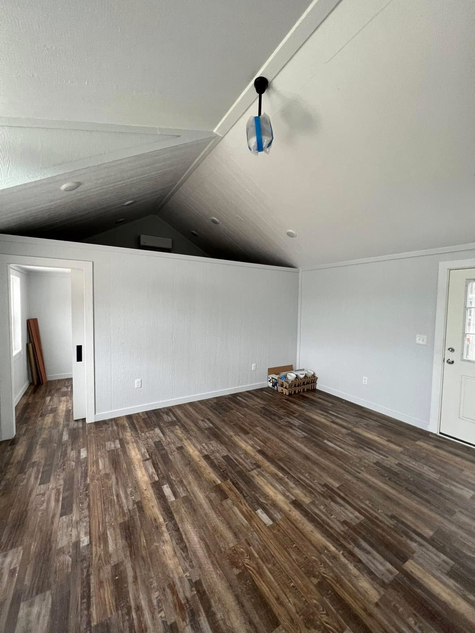 Spacious room with high vaulted ceiling, hardwood floors, and white walls. A blue pendant light hangs from the ceiling, evoking a minimalist feel.