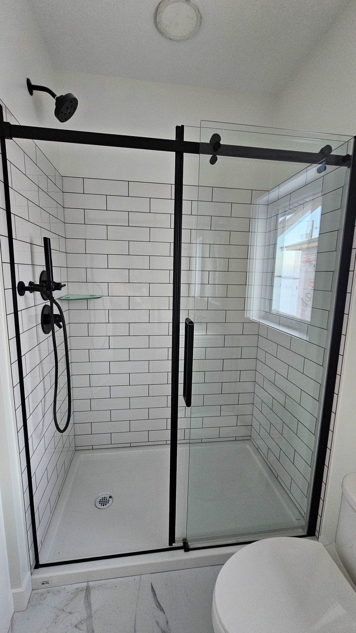 A modern bathroom features a glass-enclosed shower with white subway tiles and black fixtures. A toilet is visible, creating a sleek, clean look.