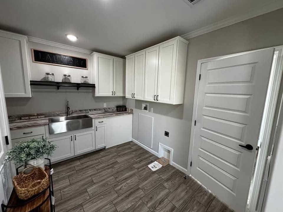 Bright laundry room with white cabinets, stainless steel sink, and wooden floor. A "Laundry" sign and potted plant add a cozy touch.