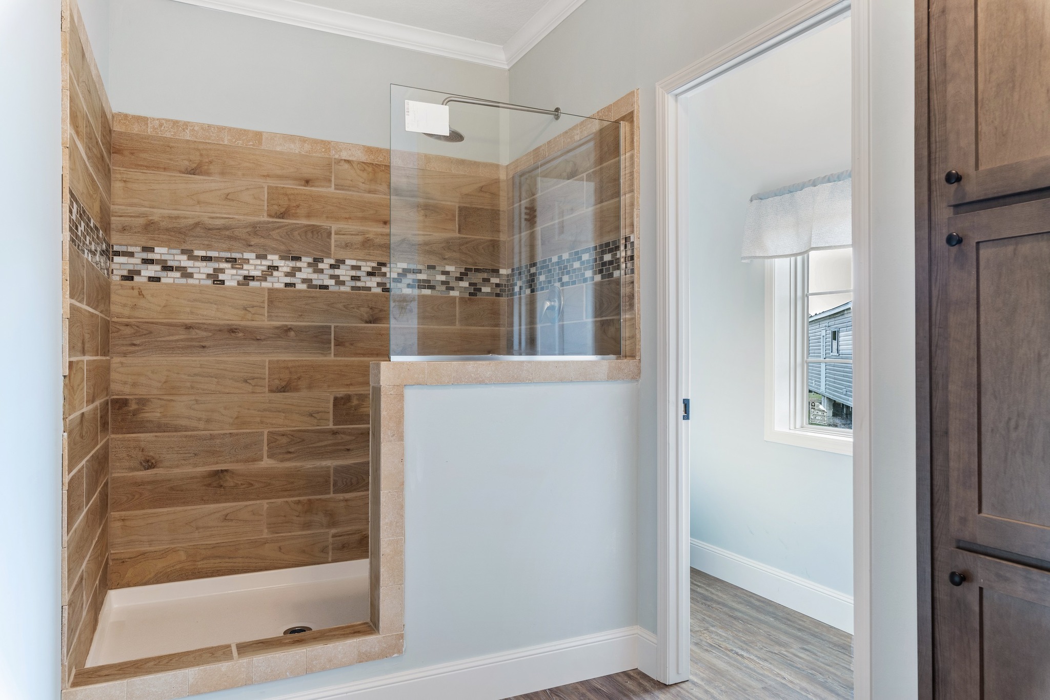 Modern bathroom with a wood-tiled shower featuring a decorative mosaic strip. Soft blue walls and natural light create a calm, inviting atmosphere.