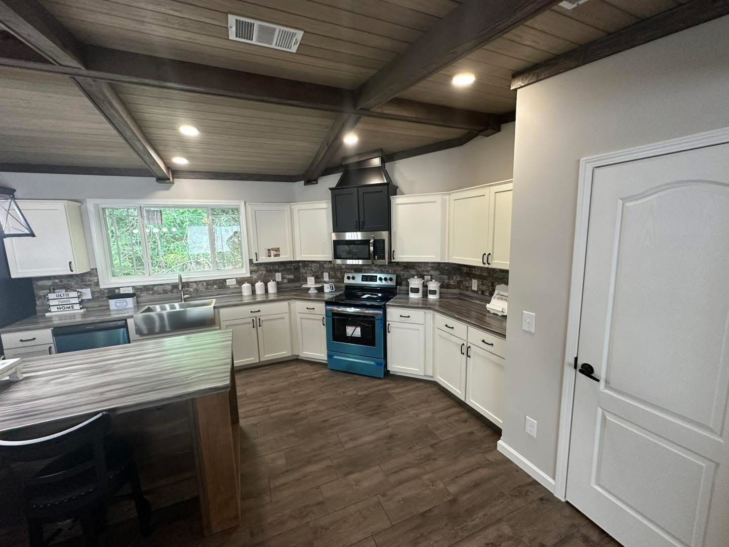 Spacious kitchen with dark wood floors, white cabinets, and a modern stove. Large window above the sink, creating a bright, inviting atmosphere.