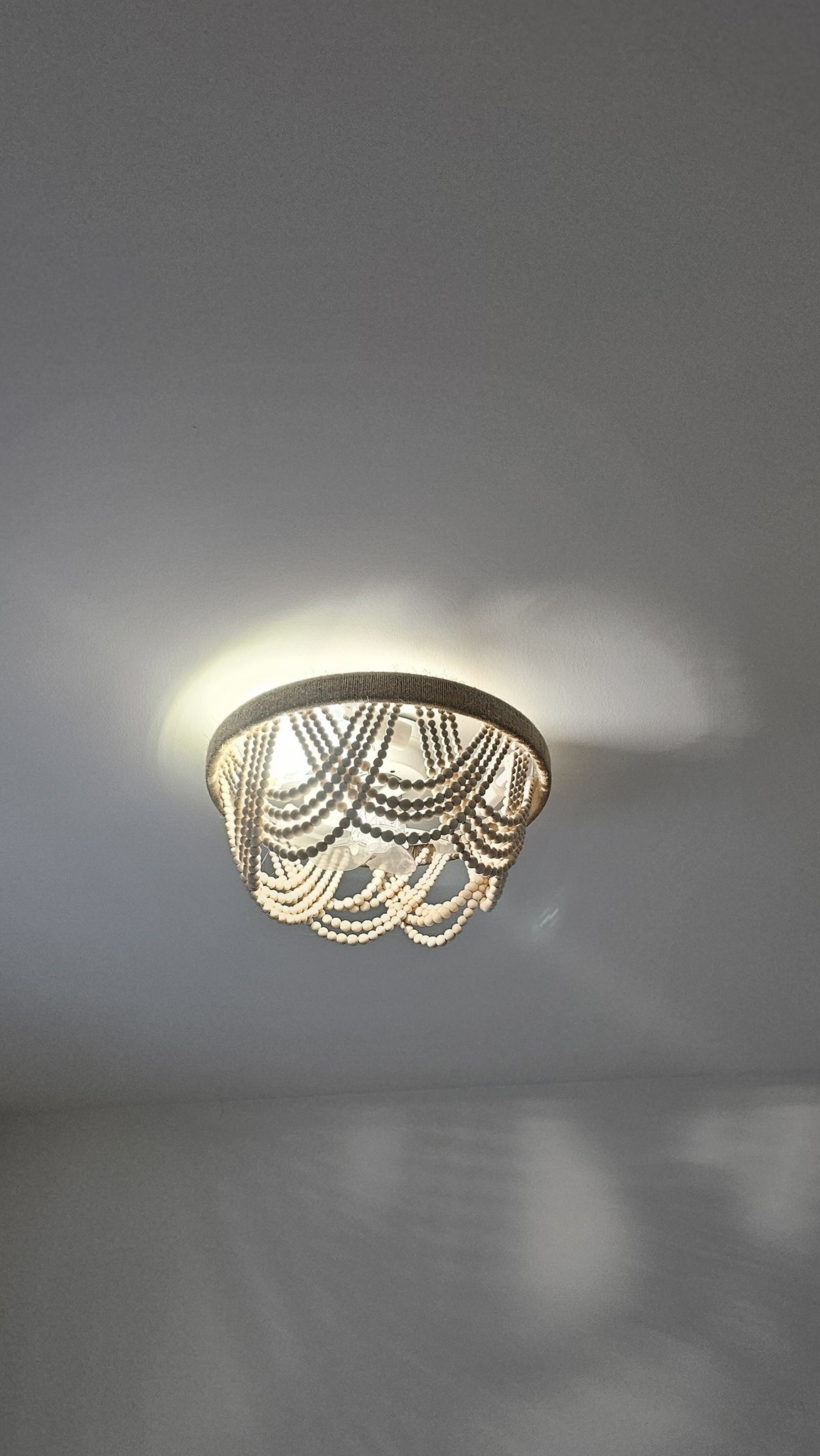 Ceiling-mounted light fixture with draped bead design casts soft shadows on a gray ceiling. The elegant, ornate style creates a warm, inviting ambiance.