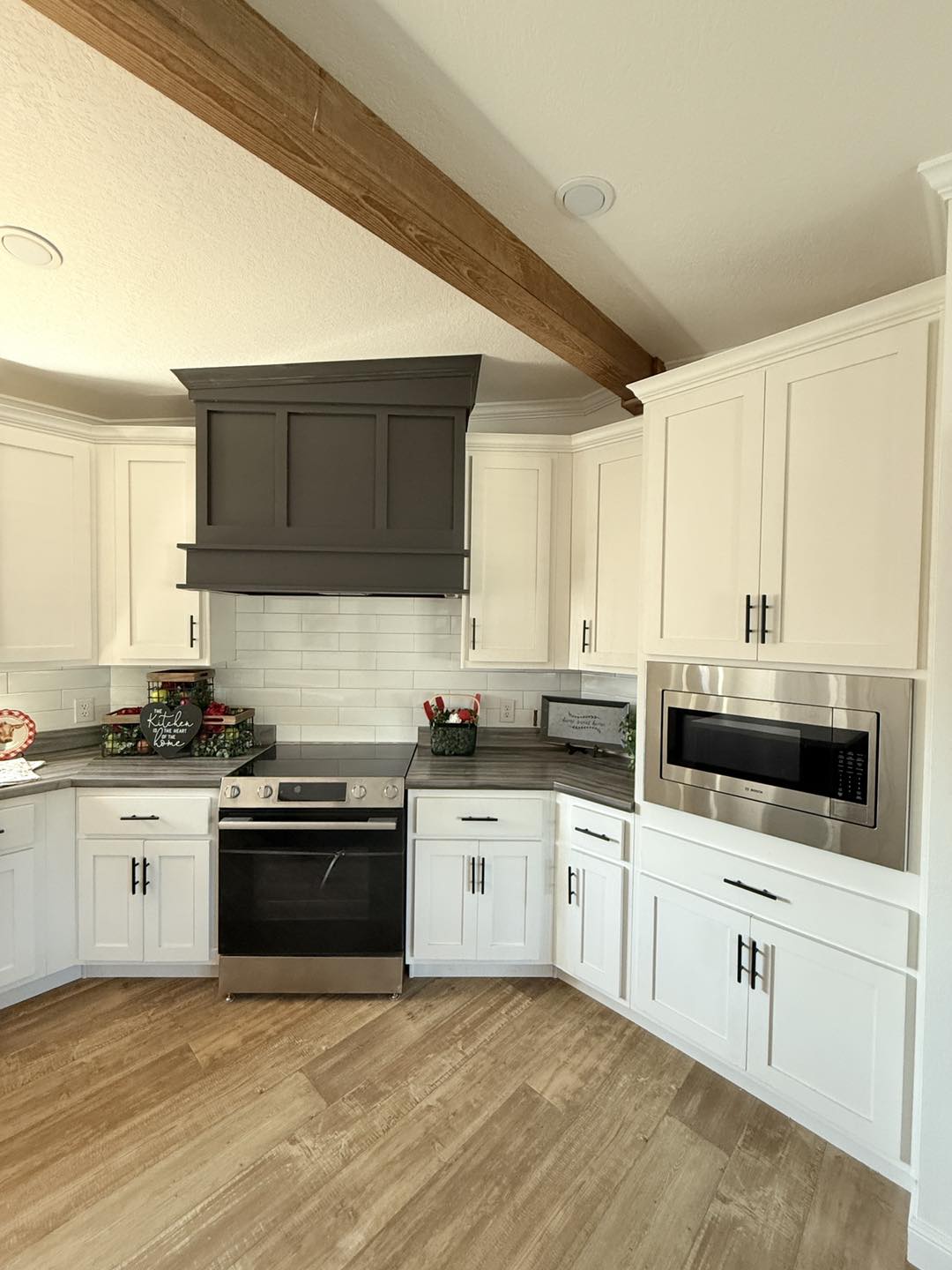 Modern kitchen with white cabinets, a dark gray range hood, and stainless steel appliances. Light wood flooring adds warmth and elegance.