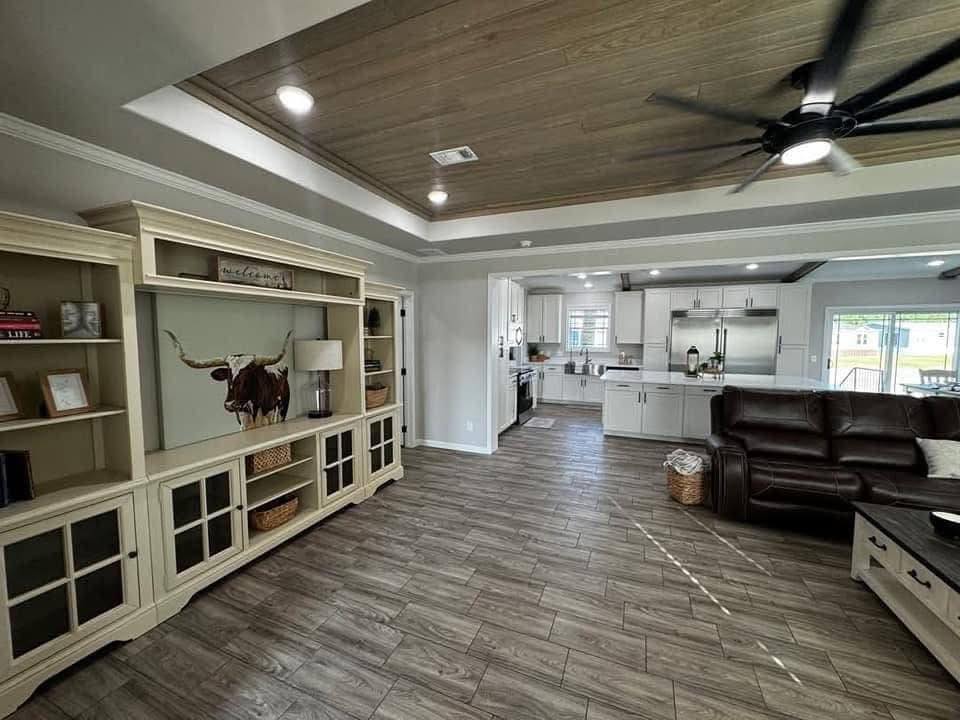 Spacious living room with wooden floors, beige shelves, a large leather sofa, ceiling fan, and an open kitchen. Bright, airy, and modern ambiance.