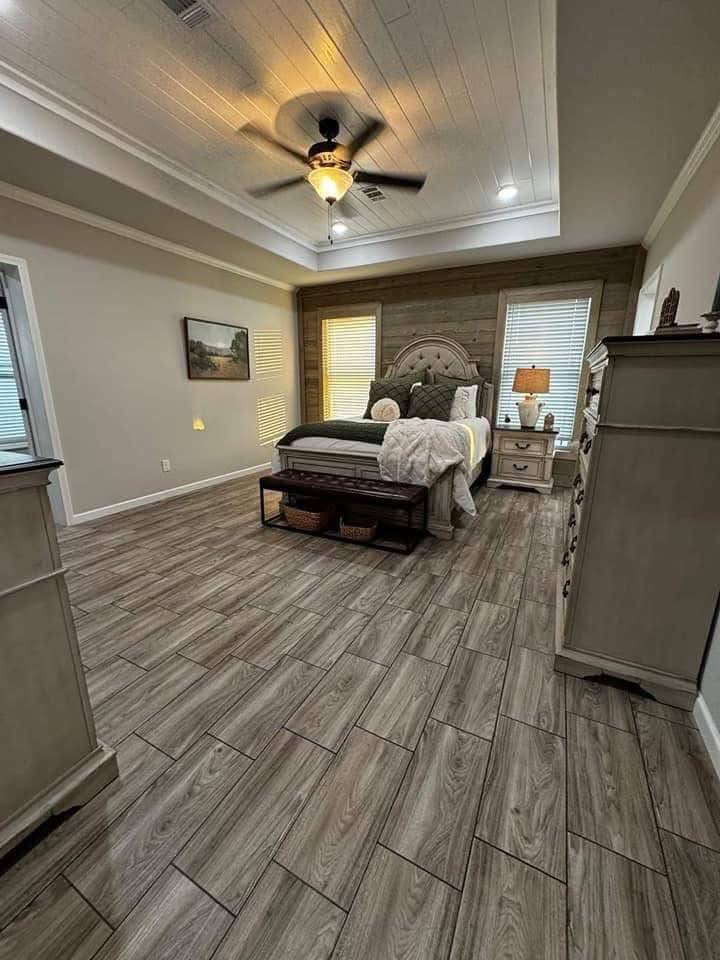 Cozy bedroom with wood-patterned tile floor and warm lighting. Features a plush bed, bedside tables, soft blankets, ceiling fan, and serene decor.