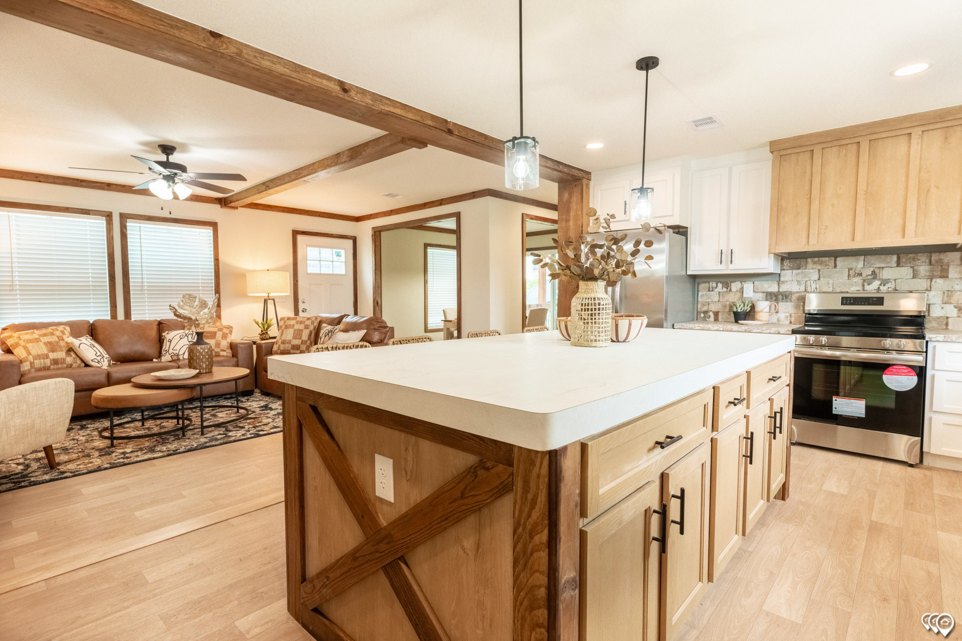Modern open-plan kitchen and living area with wooden beams and cabinetry. Cozy furnishings and neutral tones create a warm, inviting atmosphere.