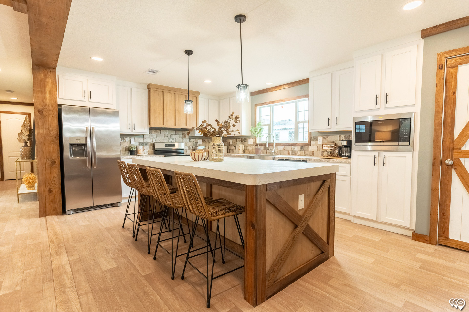 Spacious kitchen with a large island, wooden accent, wicker barstools, stainless steel appliances, white cabinets, and warm lighting, creating a cozy, inviting atmosphere.