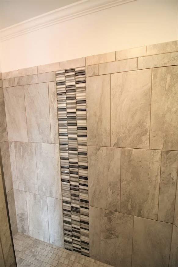 Shower wall with large beige tiles and a vertical mosaic accent strip featuring gray and black stripes, creating a modern and clean look.