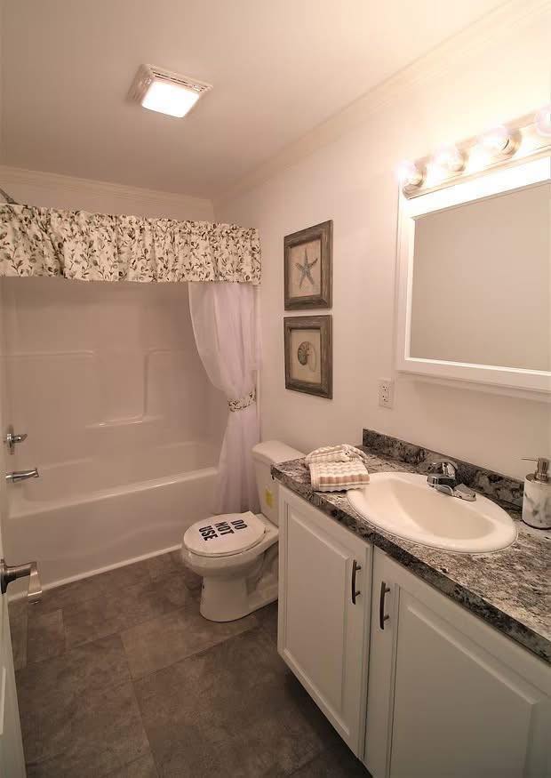 Narrow bathroom with a white tub, floral curtain, granite countertop, sink, and mirror. Walls have seashell art, creating a calm, coastal vibe.