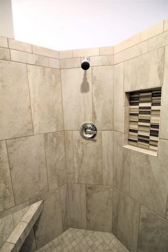 A tiled shower with beige marble tiles, featuring a wall-mounted showerhead, a small niche with dark accents for toiletries, and a corner bench, creating a clean, modern look.