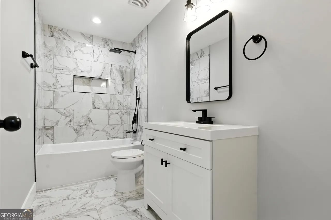 Modern bathroom featuring a white vanity with a black-framed mirror, marble-patterned tiles on the bathtub and floor, and sleek black fixtures.
