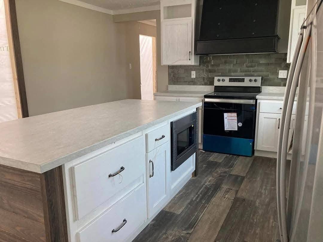 Modern kitchen with white cabinetry, dark countertops, and wood floor. Features an island with built-in microwave, stainless steel fridge, and stove.