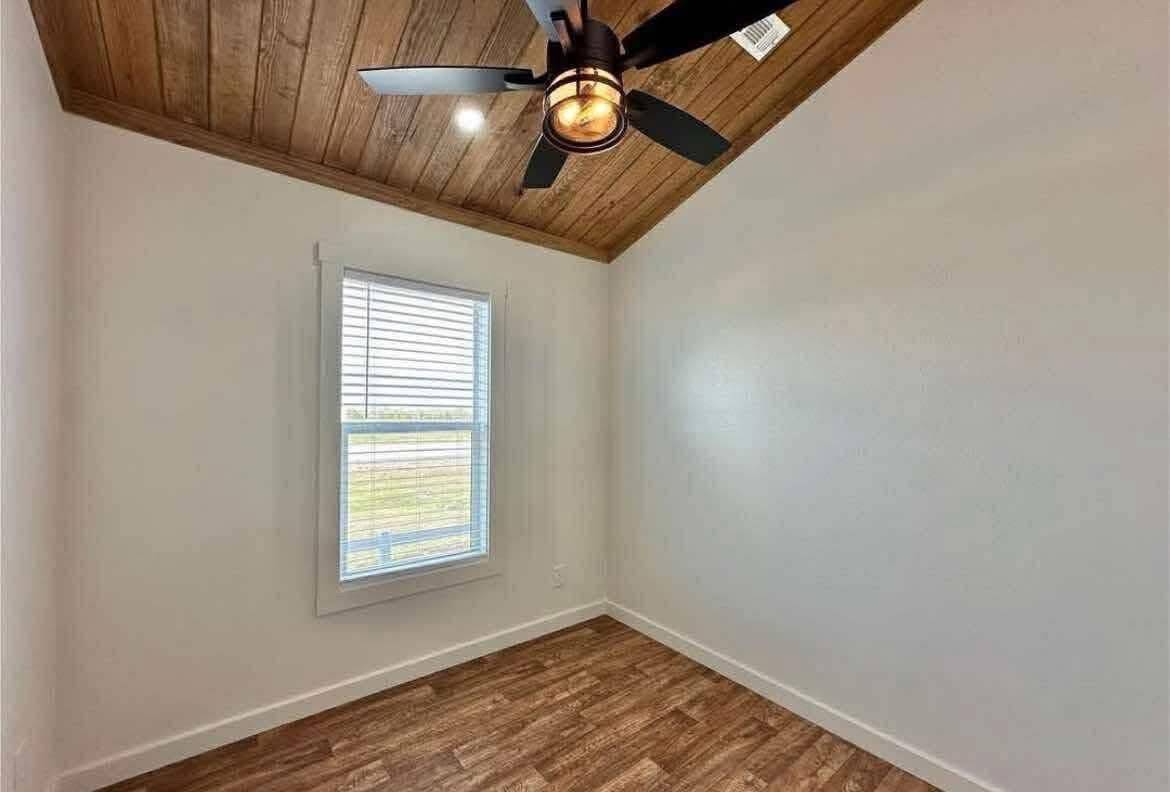 Small room with a wooden ceiling and floor, white walls, and a ceiling fan. A window with blinds lets in natural light, creating a cozy atmosphere.