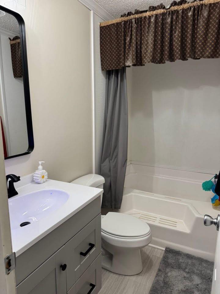 A small bathroom with a white sink and cabinet on the left, a toilet in the center, and a bathtub with gray curtains on the right. The tone is clean and simple.