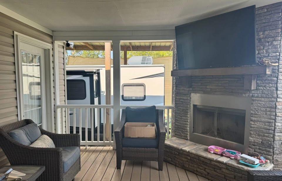 Covered patio area with wicker chairs, a fireplace, and a mounted TV. Toys and patio decor create a cozy, family-friendly atmosphere. An RV is visible outside.