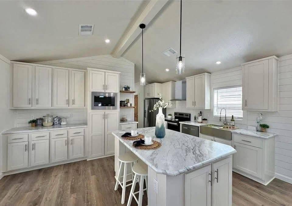 Spacious modern kitchen with white cabinets, marble countertops, and a central island. Pendant lights hang above, creating a bright, welcoming atmosphere.