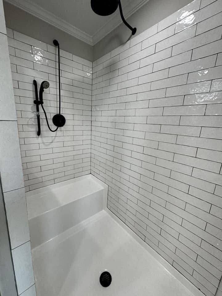 Modern shower with white subway tiles and black fixtures, including a rainfall showerhead and handheld sprayer. Clean, minimalist design.